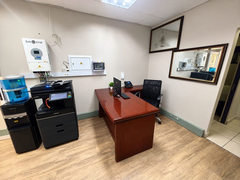 A functional office space featuring a suspended ceiling, integrated inverter system, and wall-mounted electrical distribution board with wood-look flooring.