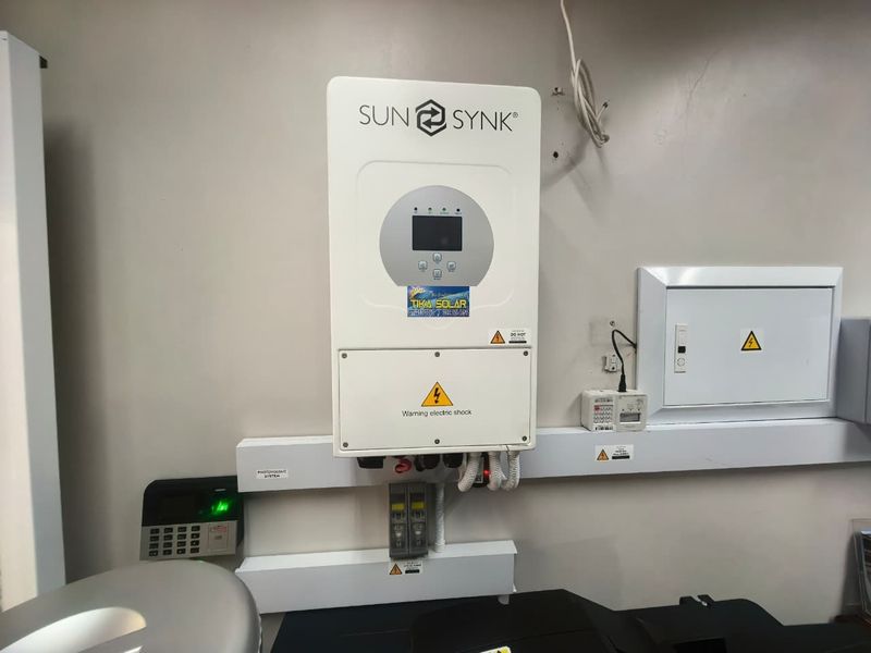 Utility area featuring a wall-mounted Sunsynk solar inverter, electrical distribution board, and security alarm system components.
