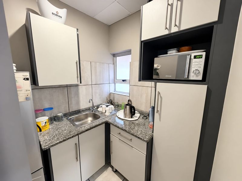 A compact and functional scullery area featuring granite countertops, stainless steel sink, and built-in cabinetry with integrated microwave storage.