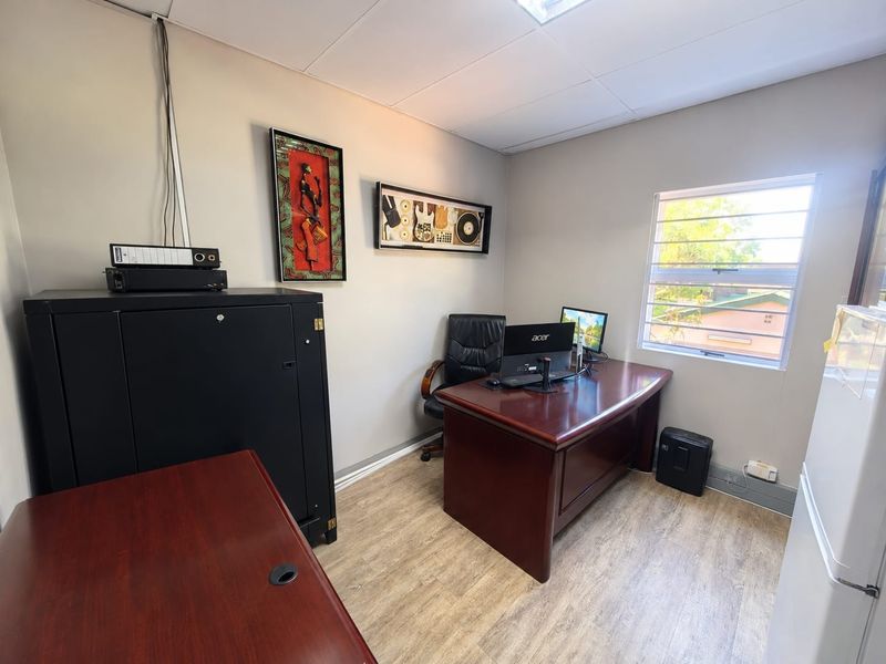 A functional office space featuring laminate flooring, a suspended ceiling, and a window with security bars, providing a practical work environment.