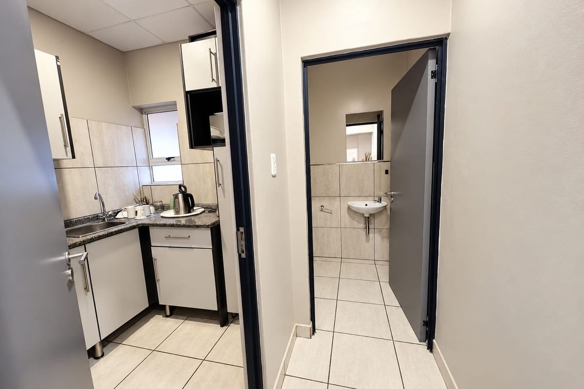 A functional office kitchenette featuring granite countertops, built-in cabinetry, and tiled finishes, with an adjacent small restroom facility.