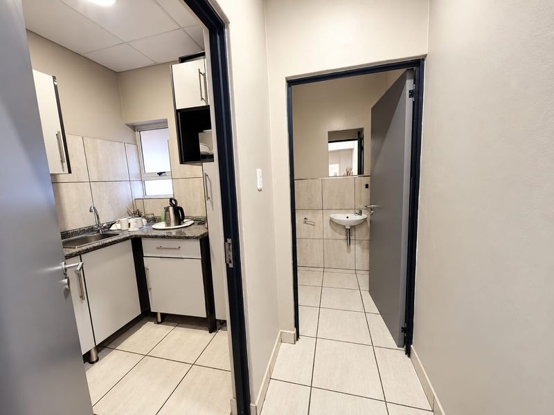 A functional office kitchenette featuring granite countertops, built-in cabinetry, and tiled finishes, with an adjacent small restroom facility.