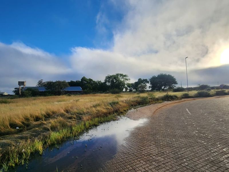A view of a vacant commercial land plot adjacent to a paved road, featuring a water tower and natural vegetation.