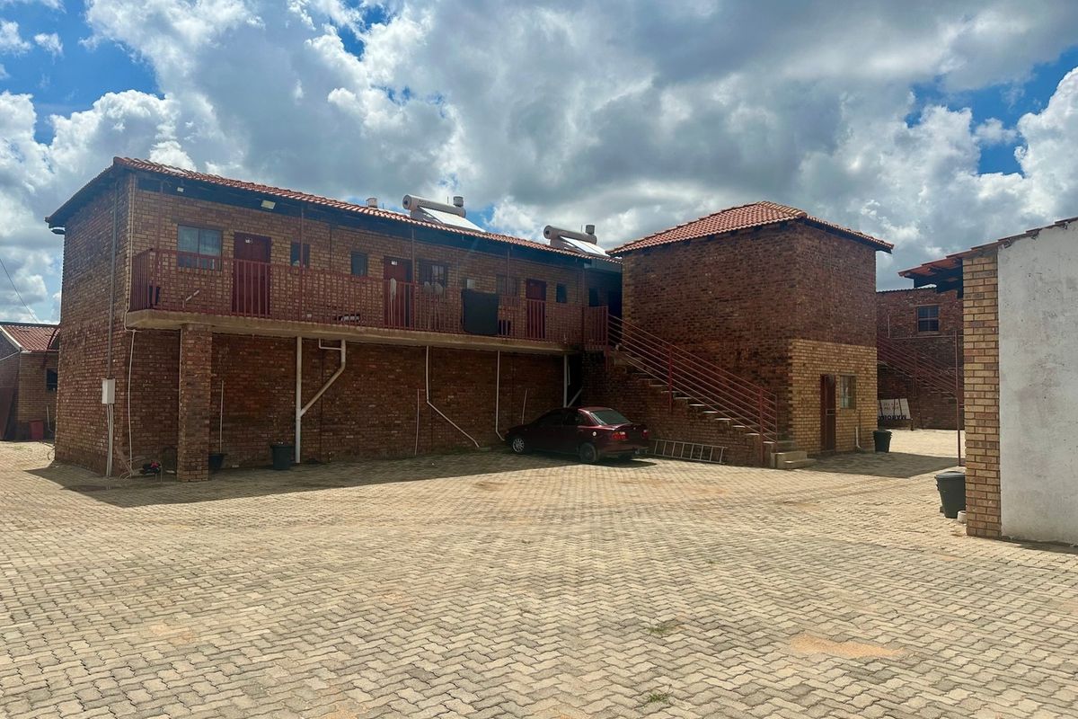Exterior view of a multi-story lodge building featuring face brick construction, tiled roofing, solar water heaters, and a paved courtyard area.