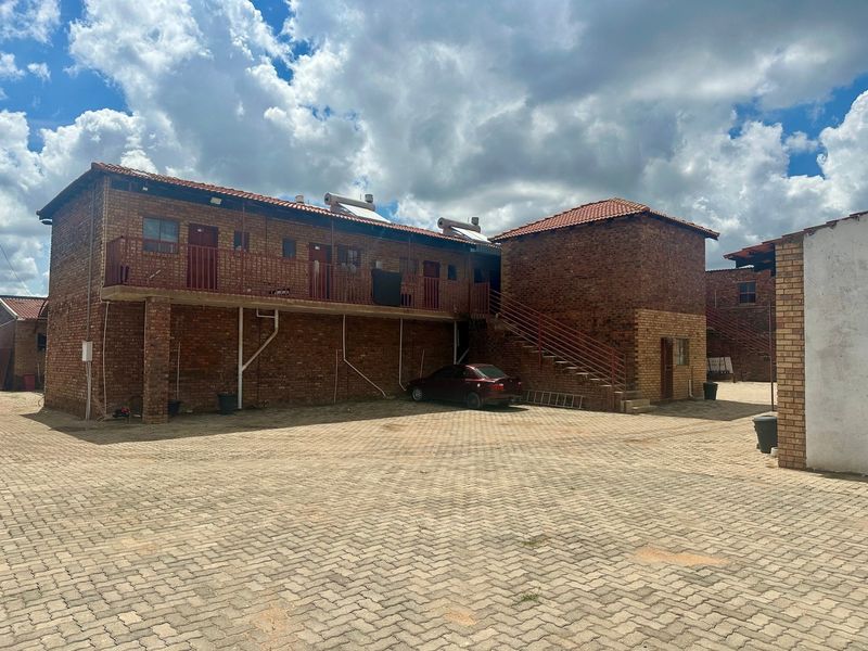 Exterior view of a multi-story lodge building featuring face brick construction, tiled roofing, solar water heaters, and a paved courtyard area.