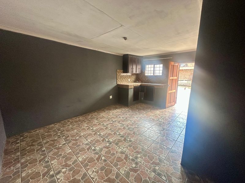 A compact, empty kitchen area featuring tiled flooring, built-in cabinetry, and a tiled backsplash, with direct access to the exterior.