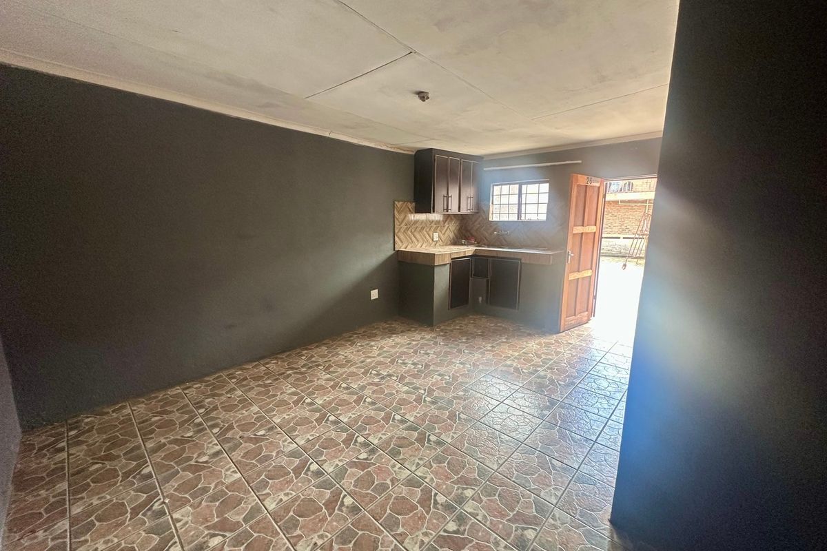 A compact, empty kitchen area featuring tiled flooring, built-in cabinetry, and a tiled backsplash, with direct access to the exterior.