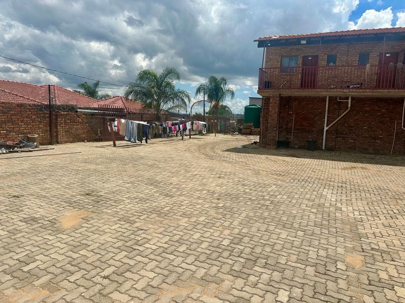 A spacious rear courtyard featuring extensive brick paving, a multi-story brick building with a balcony, and perimeter walling with security fencing.