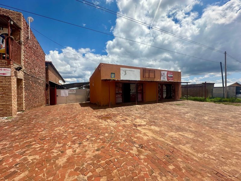 Front exterior view of a commercial lodge property featuring a large brick-paved parking area and secure gated access.