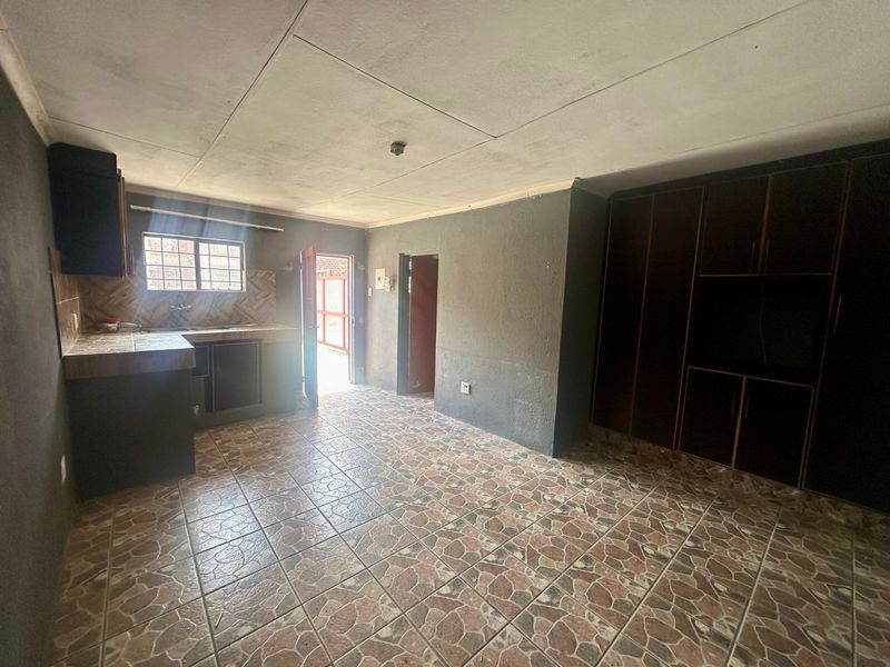 An open-plan living and kitchen area featuring tiled flooring, built-in cabinetry, and direct access to the exterior.