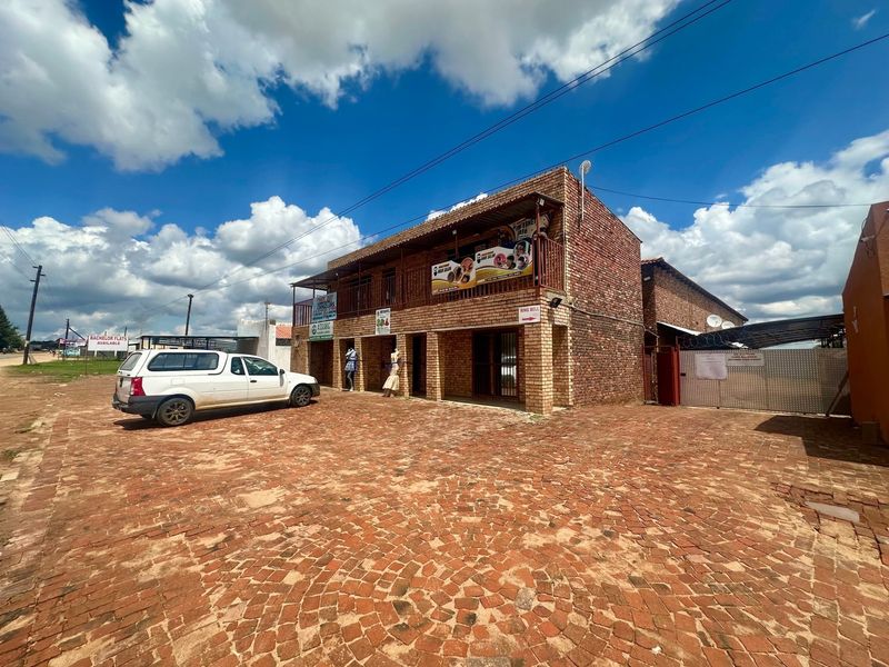 Front exterior view of a two-story brick lodge building featuring a paved driveway, balcony, and secure gated entrance.