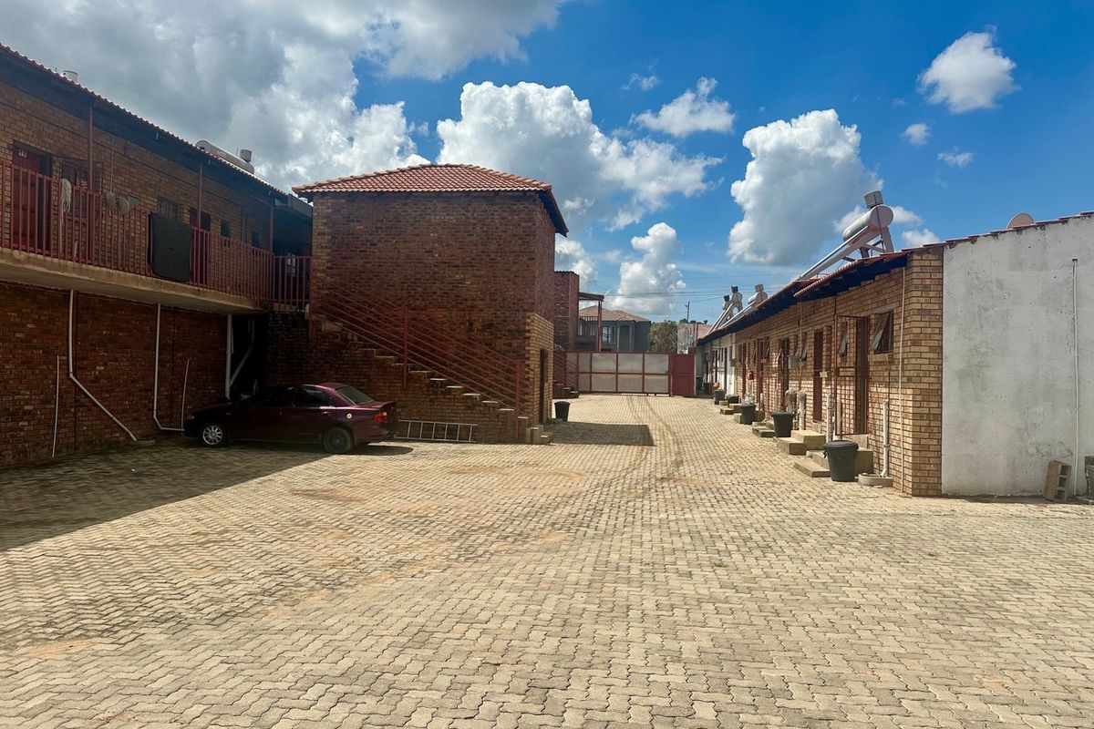 Exterior view of the lodge courtyard featuring brick buildings, paved driveway, external staircases, and solar water heating systems.
