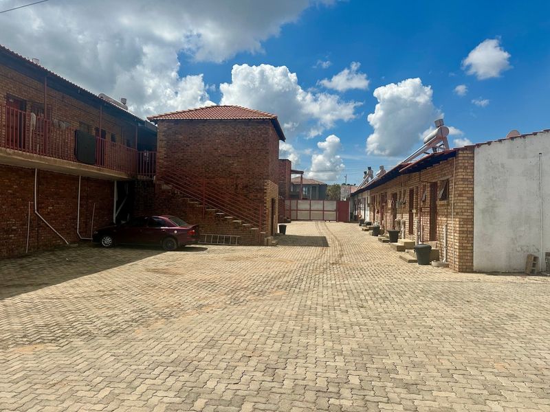 Exterior view of the lodge courtyard featuring brick buildings, paved driveway, external staircases, and solar water heating systems.
