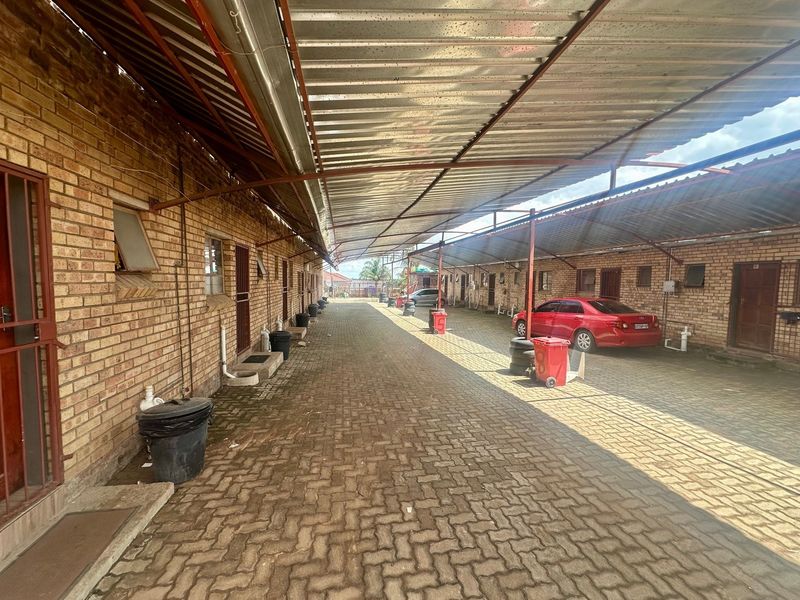 A long, paved exterior corridor featuring a covered parking area with brick building facades on both sides.