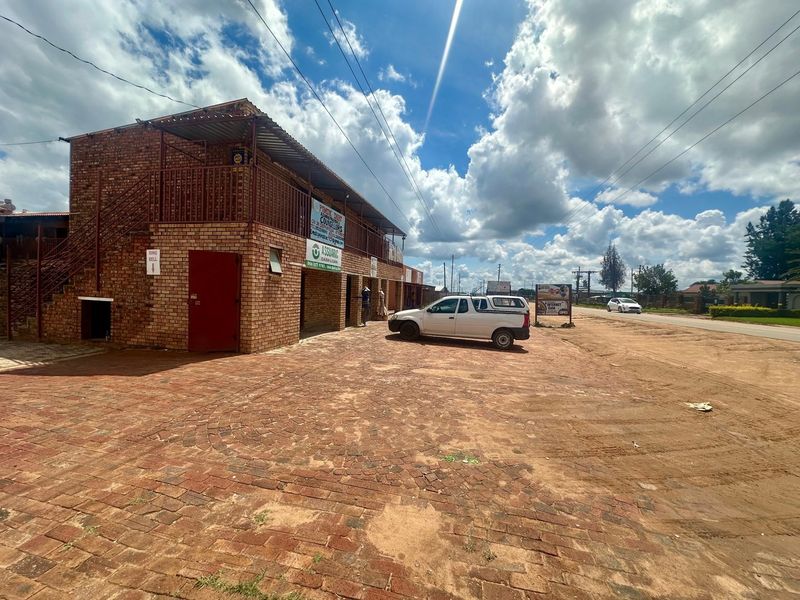 Exterior view of a multi-level face brick commercial lodge building featuring an external metal staircase, upper balcony, and a paved parking area.