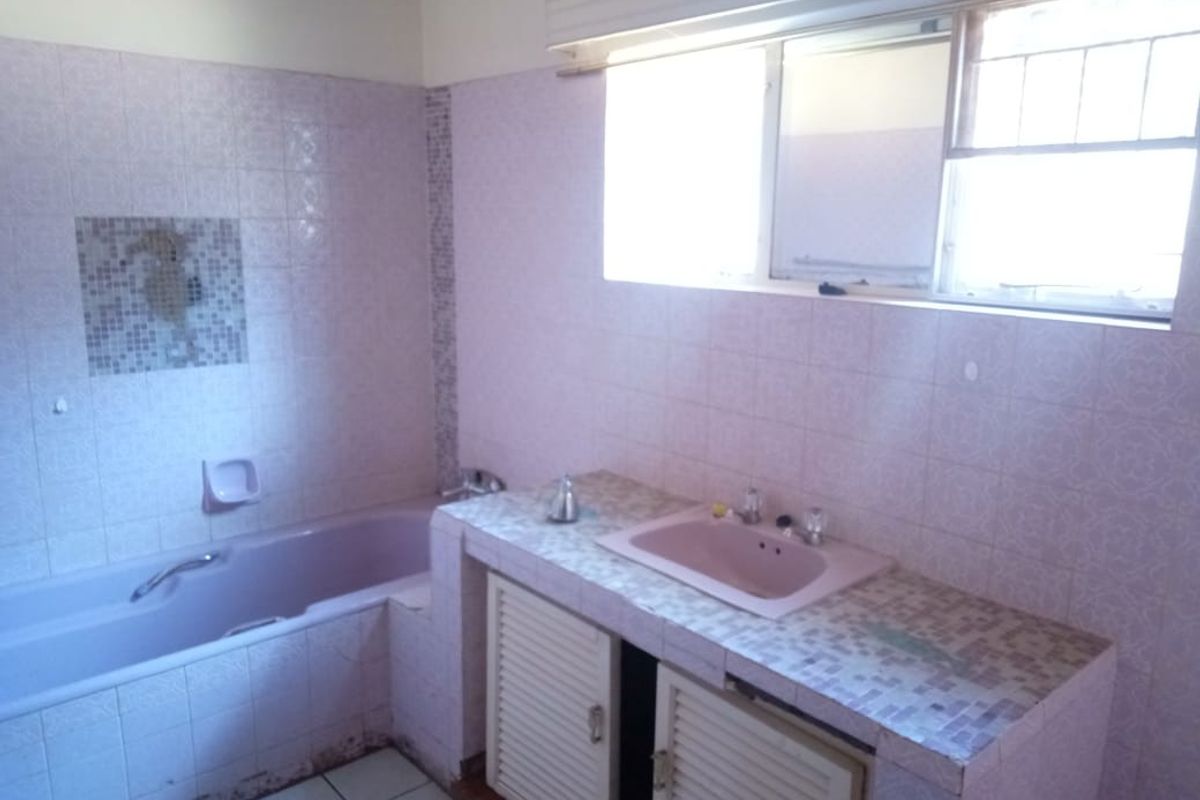 A dated bathroom featuring a built-in bathtub, tiled vanity with integrated sink, and wall-mounted window.