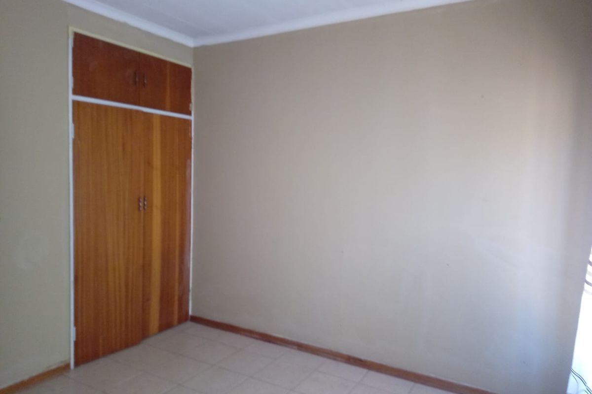 A vacant bedroom featuring built-in wooden cupboards and tiled flooring, offering a neutral canvas for personalization.