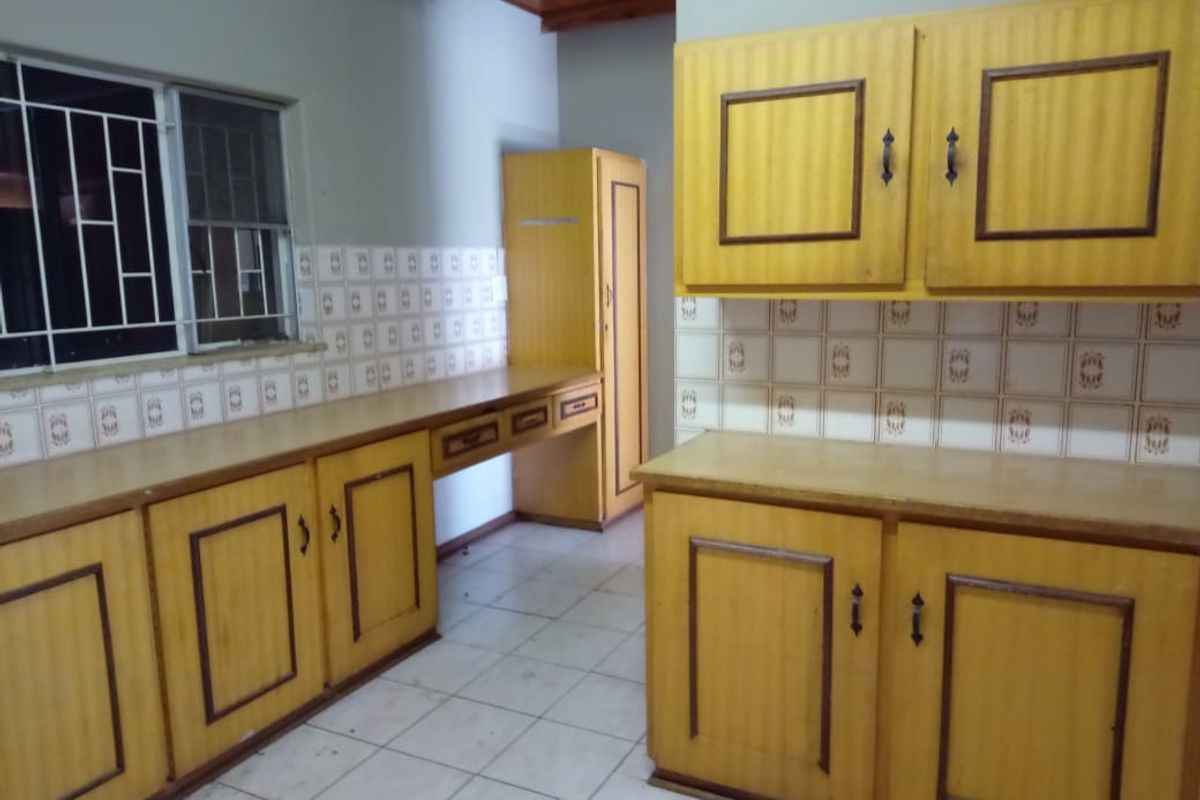 A dated kitchen featuring wooden cabinetry, tiled splashbacks, and tiled flooring, offering a functional layout ready for modernization.