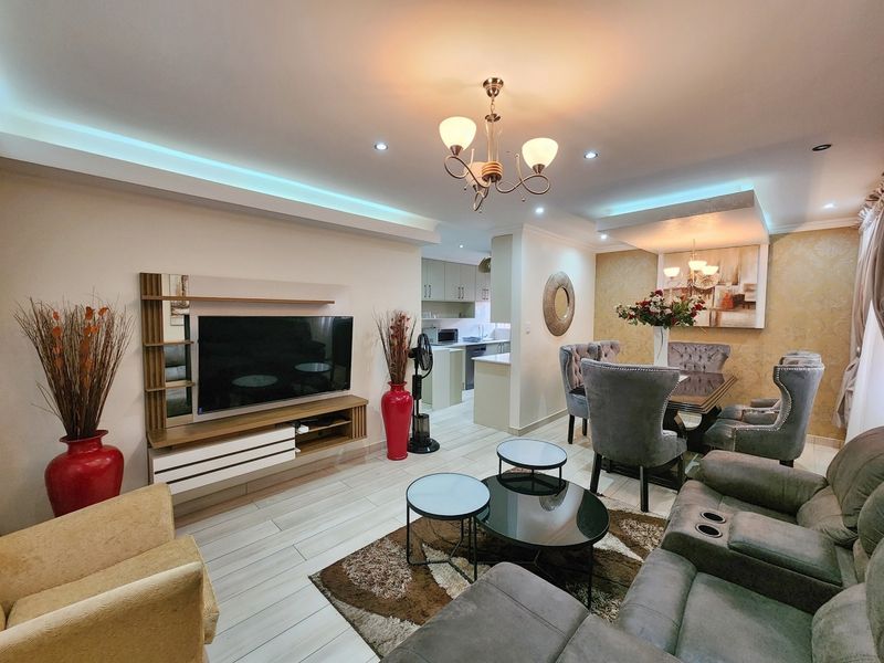 An open-plan living and dining area featuring modern tiled flooring, recessed cove lighting, and a built-in media unit, seamlessly connected to a functional kitchen.