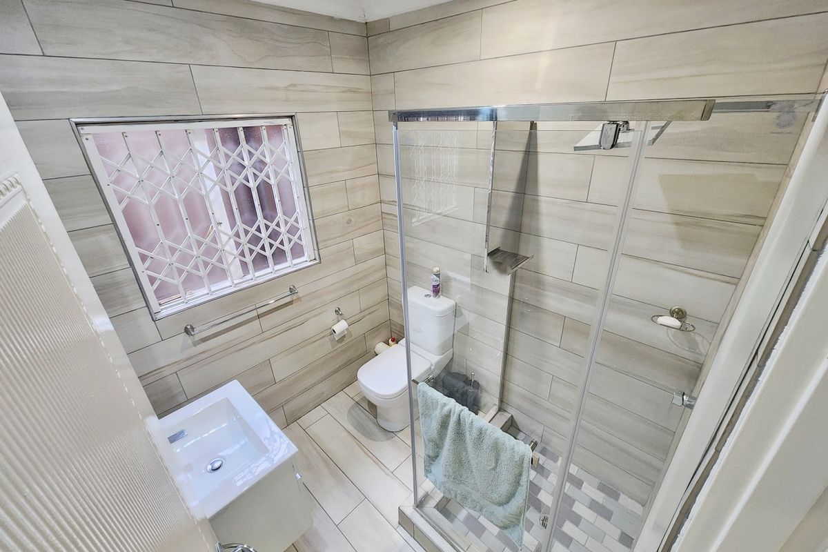 Modern bathroom featuring a glass-enclosed shower, vanity basin, toilet, and neutral wood-look wall and floor tiles.