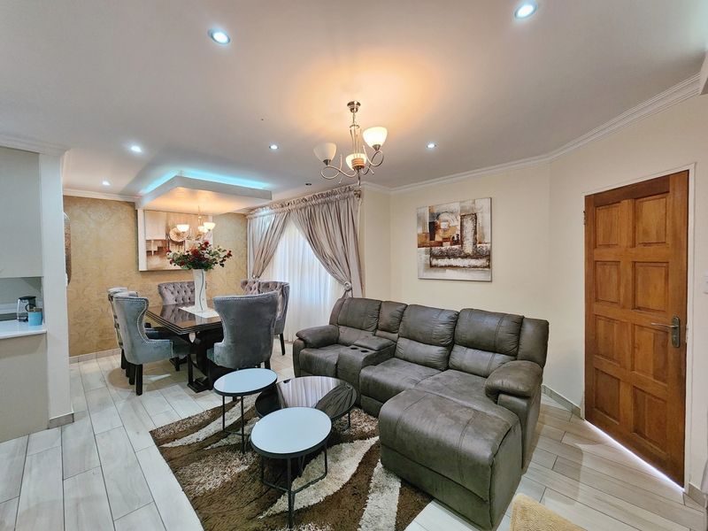 An open-plan living and dining area featuring tiled flooring, recessed ceiling lighting with cove accents, and classic crown molding.