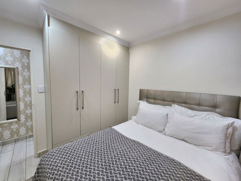 A well-maintained bedroom featuring built-in cupboards, recessed downlighting, and neutral tiled flooring, offering a clean and functional living space.