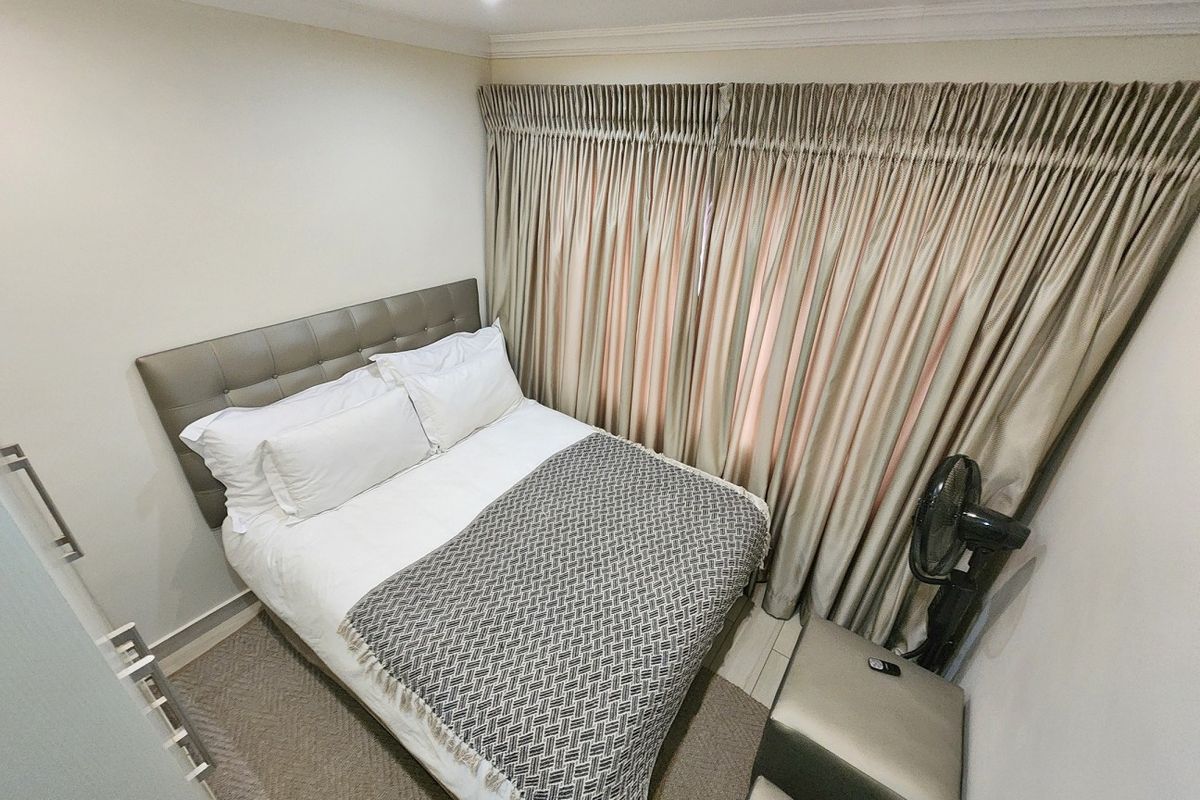 A compact, well-maintained bedroom featuring neutral wall tones, recessed ceiling lighting, and full-length window drapery.