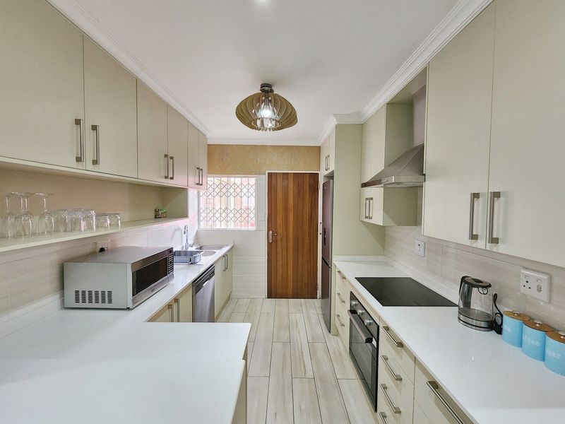 A well-maintained galley kitchen featuring modern cabinetry, stone countertops, integrated appliances, and tiled flooring with a rear access door.