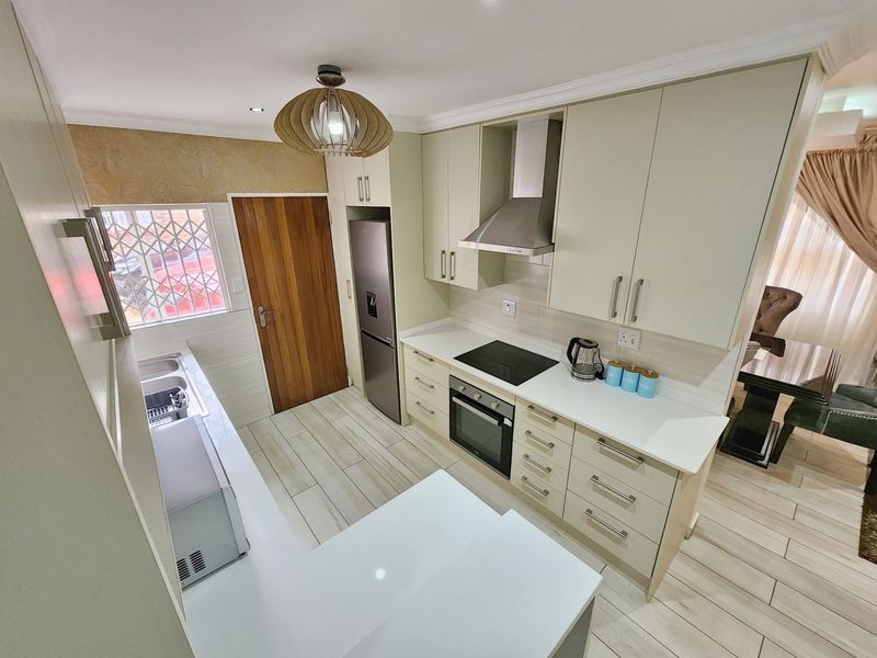 Modern kitchen featuring light-toned cabinetry, stone countertops, integrated electric hob and oven, stainless steel extractor, and tiled flooring with a functional layout.