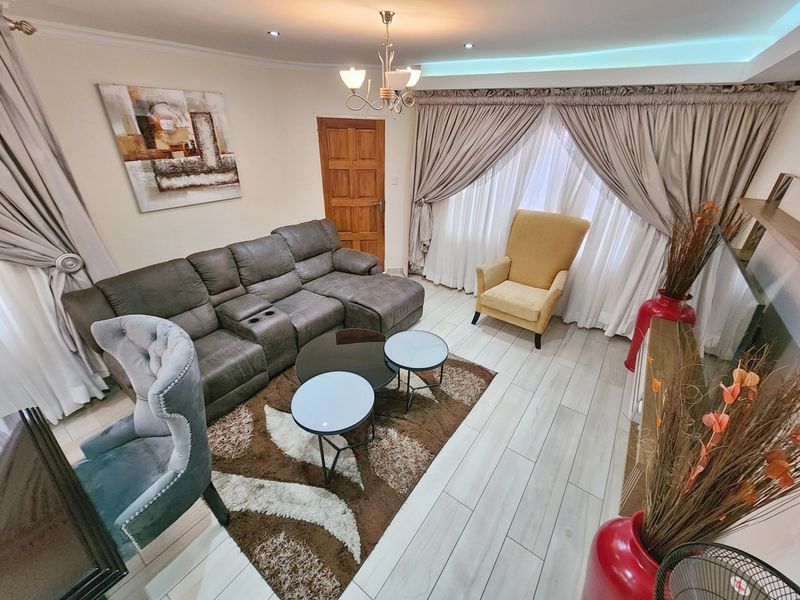 A well-maintained living room featuring tiled flooring, recessed downlighting, and cove lighting, creating a bright and comfortable atmosphere.