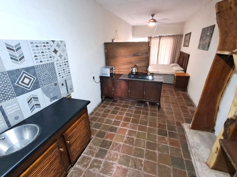 Open-plan studio apartment featuring terracotta tile flooring, a compact kitchenette with patterned splashback tiles, and a combined living and sleeping area.