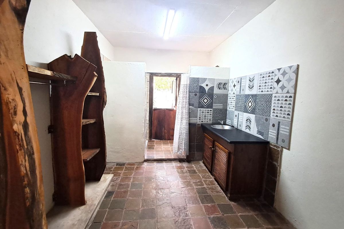 A functional laundry area featuring built-in cabinetry, a sink, decorative tiled splashback, and direct access to an outdoor space.