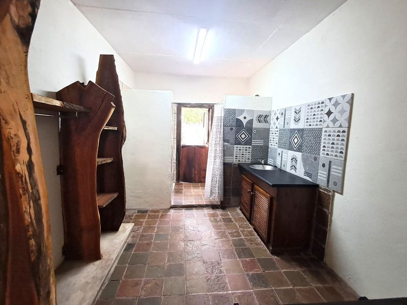 A functional laundry area featuring built-in cabinetry, a sink, decorative tiled splashback, and direct access to an outdoor space.
