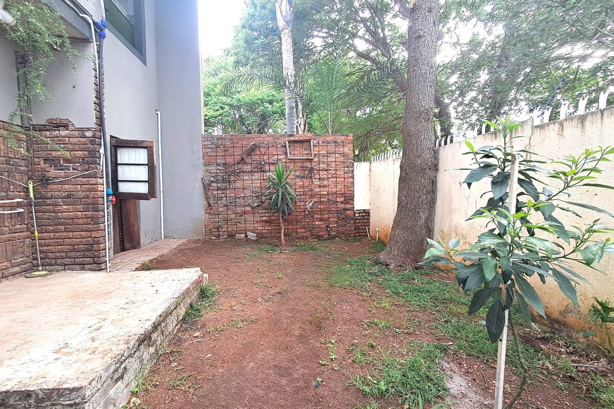 A private rear garden area featuring a concrete patio, exposed brick boundary walls, and established trees, offering potential for landscaping and outdoor improvement.