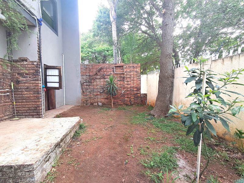 A private rear garden area featuring a concrete patio, exposed brick boundary walls, and established trees, offering potential for landscaping and outdoor improvement.