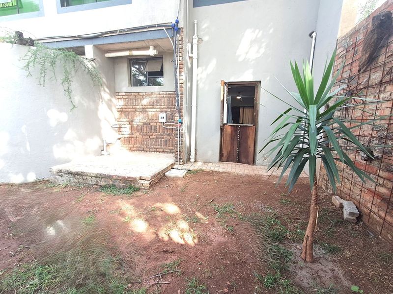 Rear exterior view of the apartment featuring a small paved patio area, exposed brickwork, and a stable-style door leading into the unit.