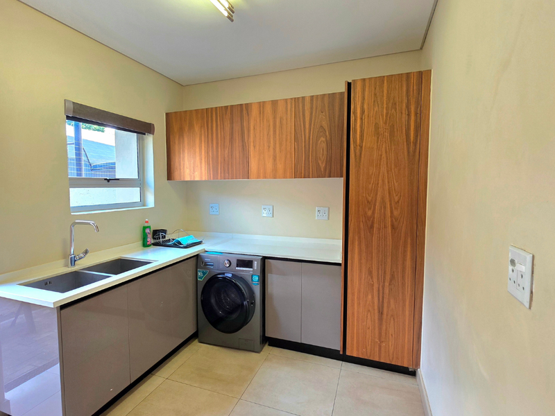 A functional laundry room featuring modern wood-finish cabinetry, ample counter space, a double sink, and tiled flooring.