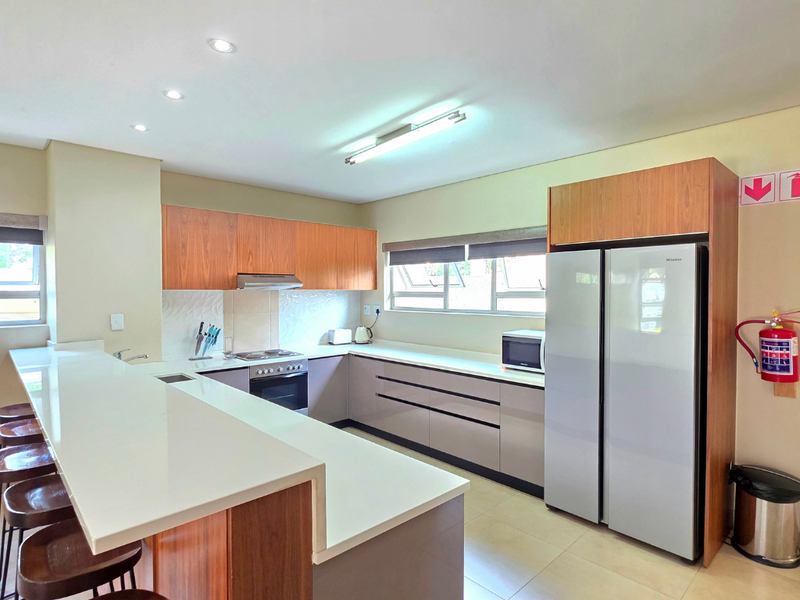 Modern kitchen featuring wood-tone and neutral cabinetry, stone countertops, a breakfast bar, and integrated appliances, offering a clean and functional workspace.
