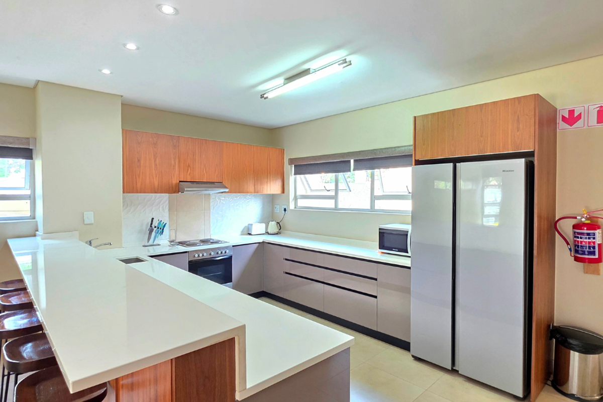 Modern kitchen featuring wood-tone and neutral cabinetry, stone countertops, a breakfast bar, and integrated appliances, offering a clean and functional workspace.