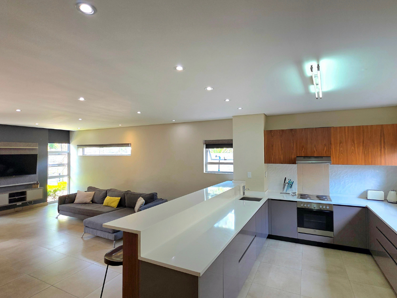 Modern open-plan living area featuring a sleek kitchen with built-in appliances, a central island, and spacious lounge area with tiled flooring throughout.