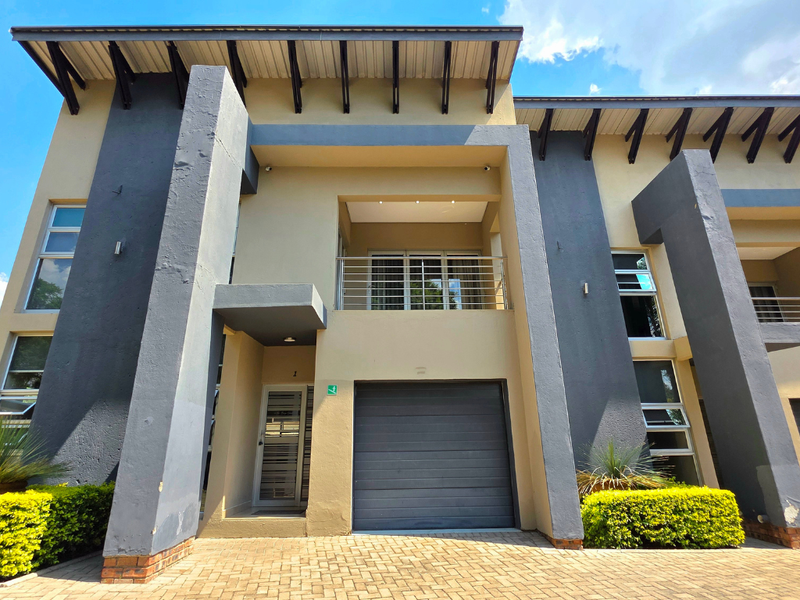 Modern townhouse facade featuring a paved driveway, single garage, and an upper-level balcony with stainless steel railings and contemporary architectural detailing.
