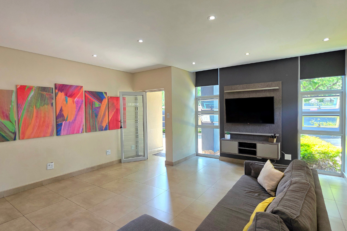 A bright and modern living room featuring tiled floors, recessed lighting, and a built-in media console with large windows providing natural light.