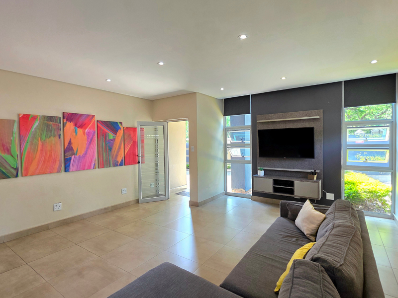 A bright and modern living room featuring tiled floors, recessed lighting, and a built-in media console with large windows providing natural light.