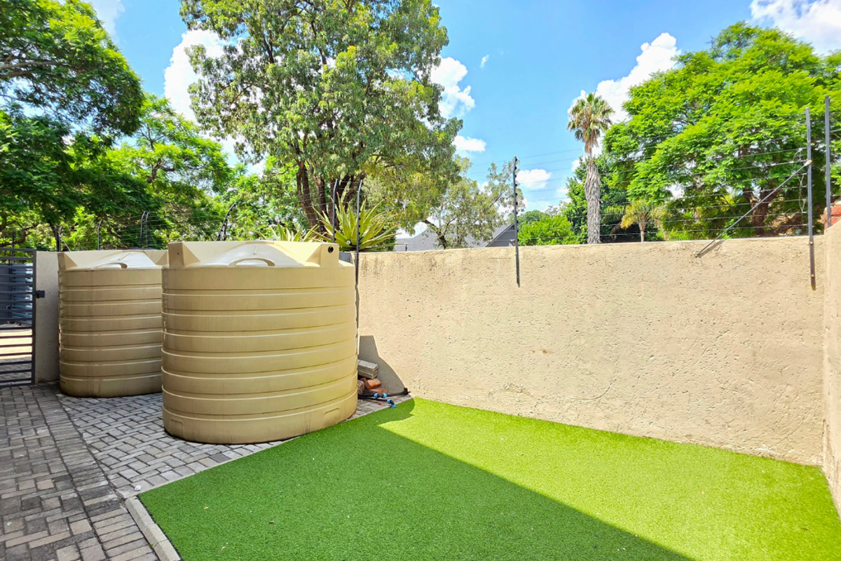 Rear courtyard area featuring two large water storage tanks, artificial grass, paved flooring, and secure boundary walls with electric fencing.