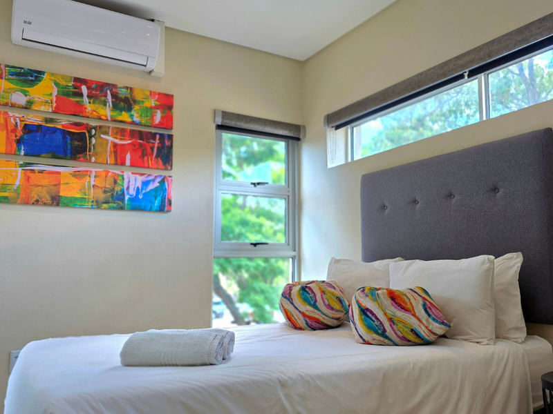 A well-maintained bedroom featuring a wall-mounted split-system air conditioner, modern aluminium window frames, and neutral wall finishes.