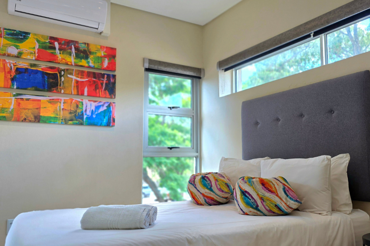 A well-maintained bedroom featuring a wall-mounted split-system air conditioner, modern aluminium window frames, and neutral wall finishes.