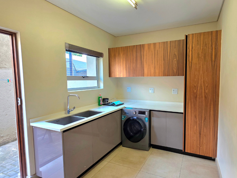 A functional laundry room featuring modern built-in cabinetry, stone countertops, a double sink, and tiled flooring with direct access to an outdoor area.
