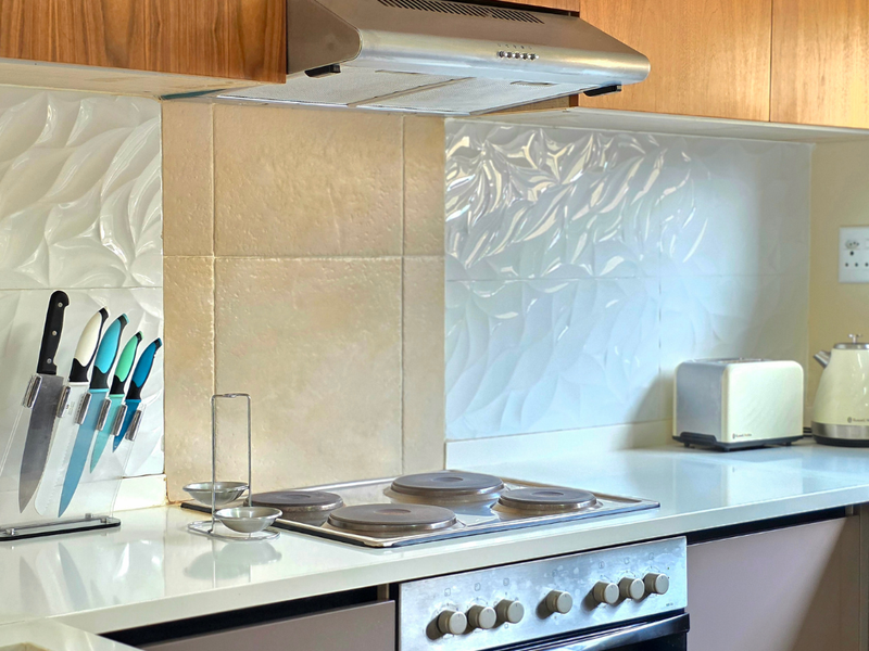 A well-maintained kitchen area featuring a built-in electric hob, oven, stainless steel extractor fan, and decorative textured tile backsplash with ample counter space.