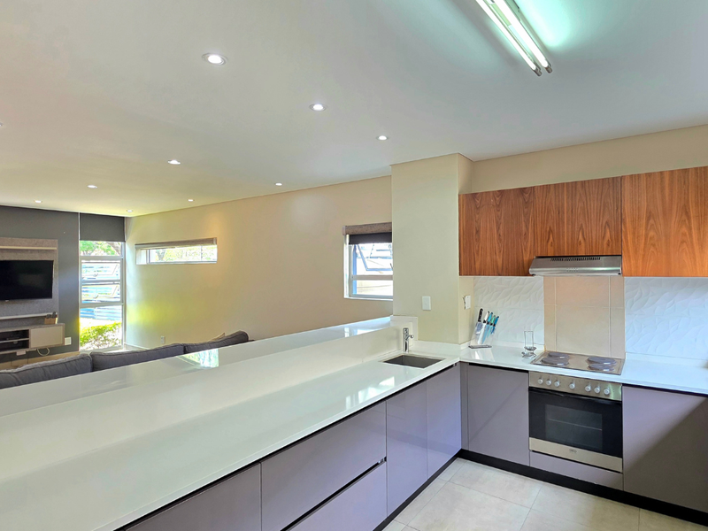 Modern open-plan kitchen featuring sleek cabinetry, stone countertops, and integrated appliances, seamlessly flowing into the adjacent living area with recessed lighting.