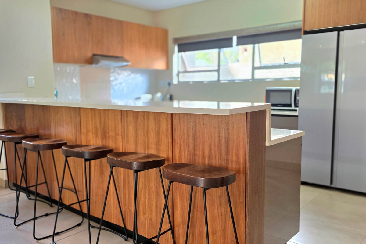 Modern kitchen featuring warm wood cabinetry, a spacious stone breakfast bar, and tiled flooring, offering a functional and contemporary cooking and dining space.